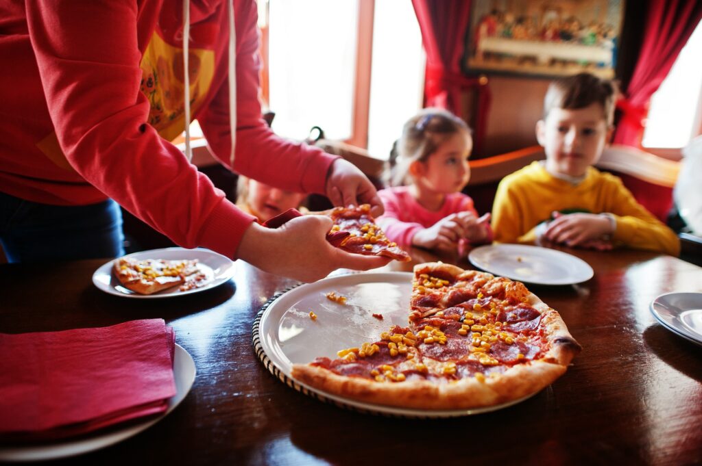 Children on birthdays sitting at the table and eating pizza.